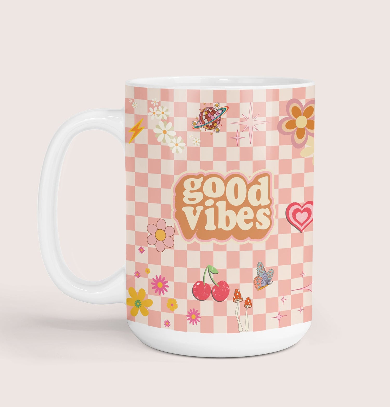 A white ceramic mug with a pink checkered pattern and various colorful illustrations, such as flowers, cherries, mushrooms, butterflies and the text 'good vibes' in the center.